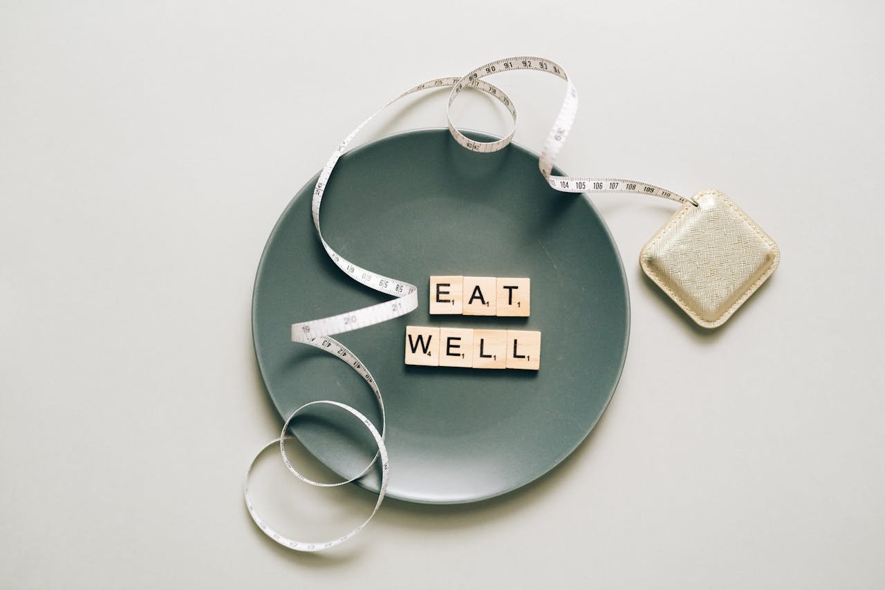 Flat lay of scrabble tiles spelling eat well on a plate with a tape measure, promoting healthy eating.
